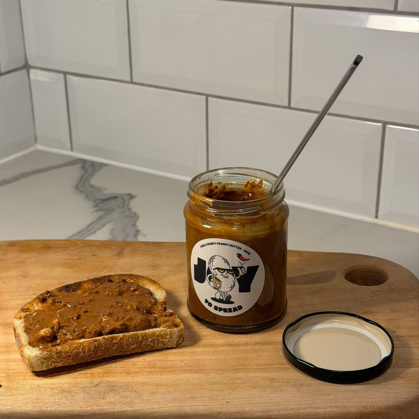 Chilli honey peanut butter spread thickly across a slice of toast, the open jar behind it
